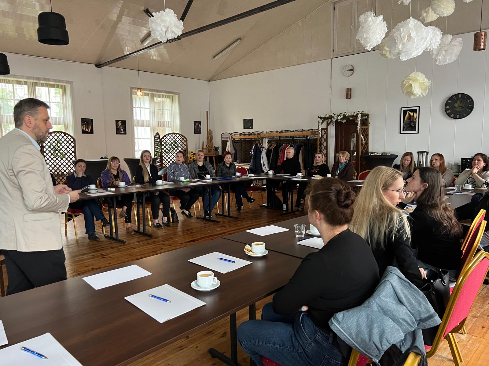 Uczestnicy szkolenia siedzą przy stole i słuchają wykładowcy